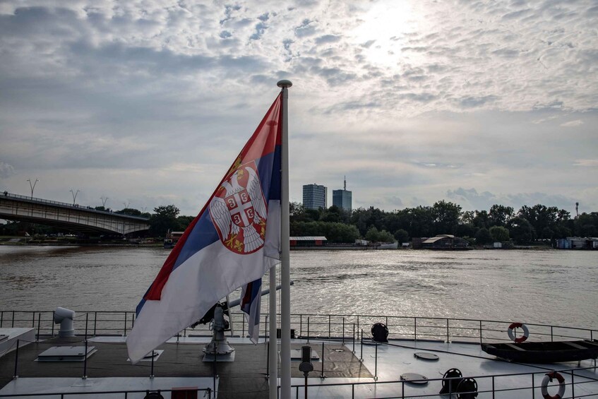 A river with a bridge in the background, a flag on a boat, and buildings along the riverbank. 4