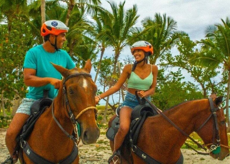 Two people riding horses on a beach with palm trees in the background. 3