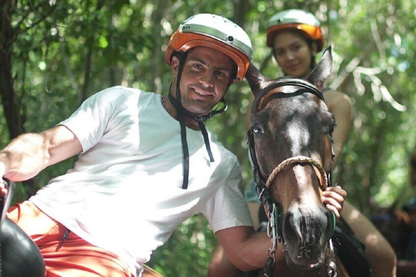 Two people riding horses in a forested area. 1