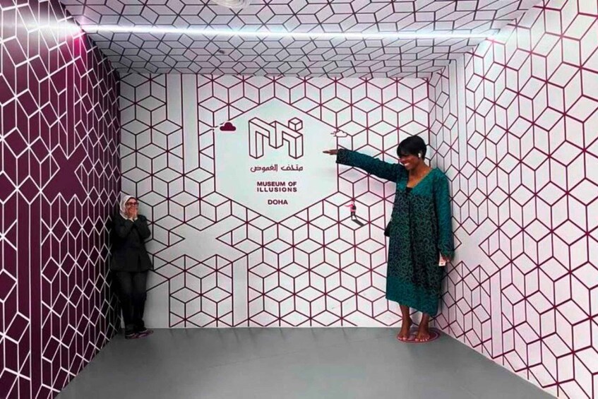 A person pointing at a wall with a geometric pattern and the text 'Museum of Illusions Doha'. 2