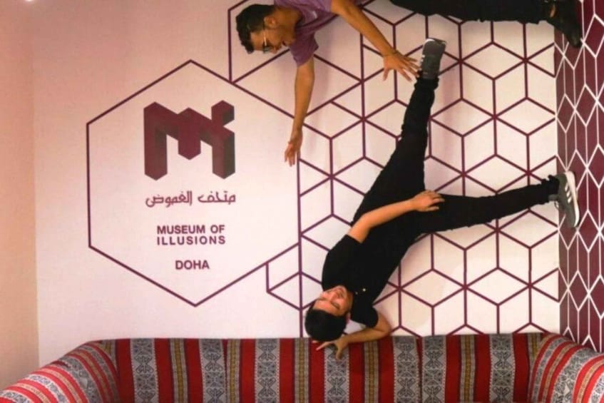 A person performing a handstand against a wall with a geometric pattern and a sign for the Museum of Illusions in Doha. 4