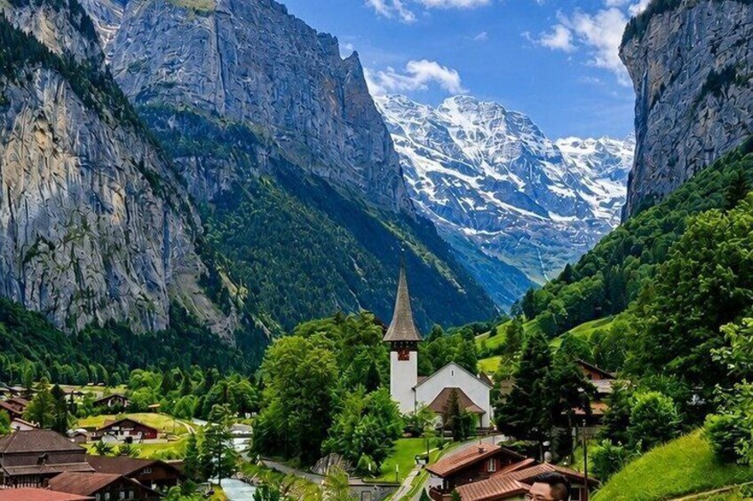 A mountainous village with a church, lush greenery, and snow-capped peaks in the background. 1