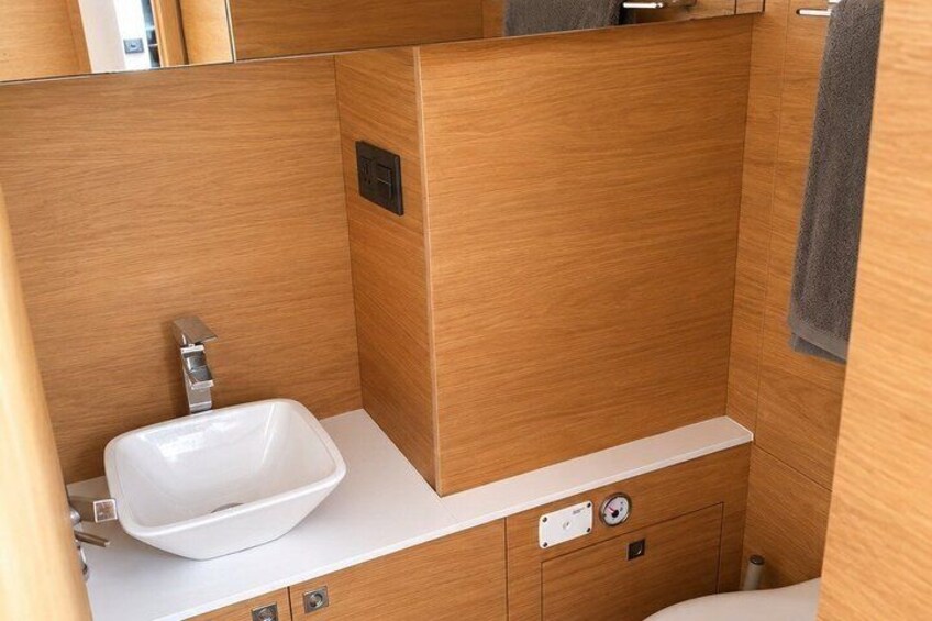 A compact bathroom with a white sink, wooden paneling, and a towel hanging on the wall. 5