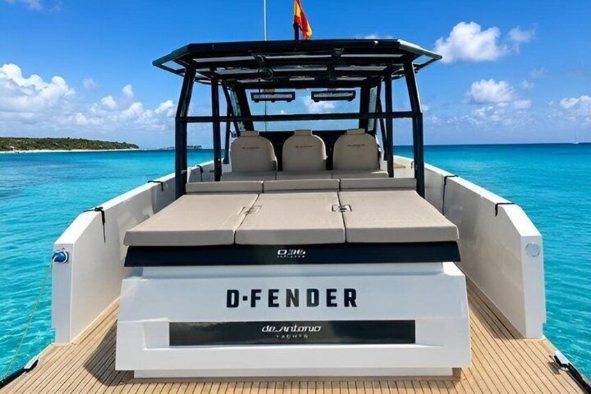 A boat named 'D-FENDER' with a covered seating area and a flag on top, on a calm sea with clear skies. 1