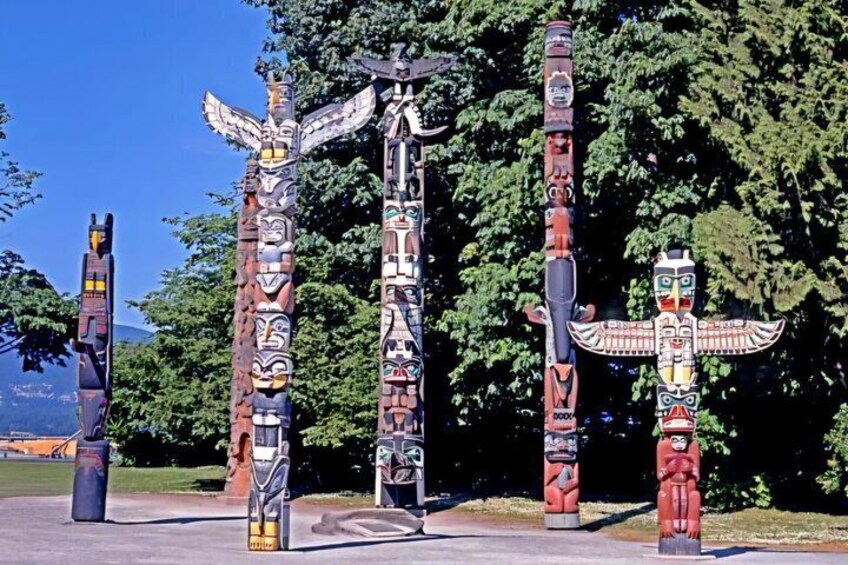 Totem poles with intricate carvings and figures, set against a backdrop of trees and a clear sky. 2