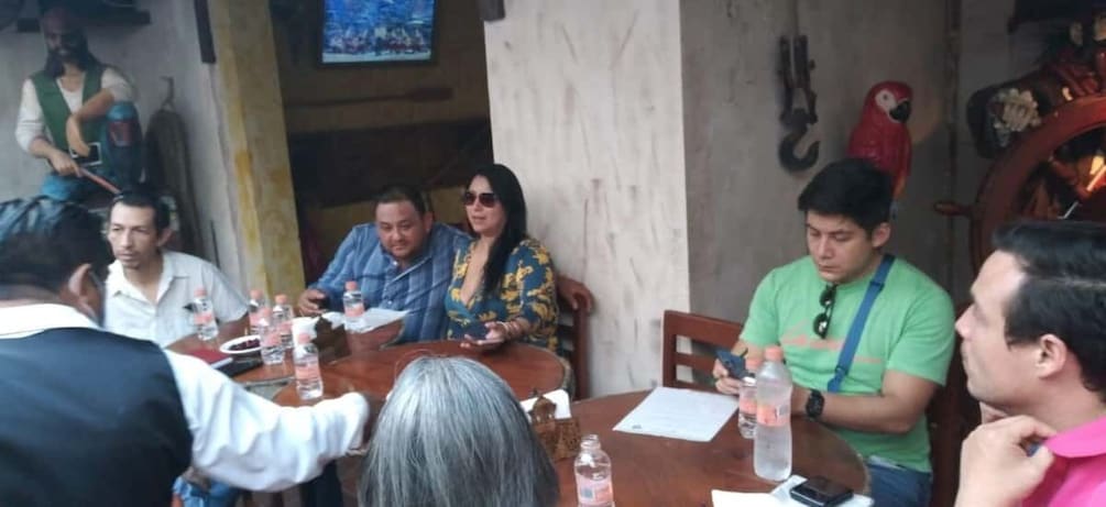 A group of people seated at a wooden table with papers and bottles of water. 3