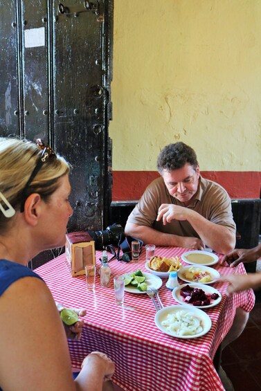 A person sitting at a table with a red and white checkered tablecloth, plates of food, and a camera on the table. 2