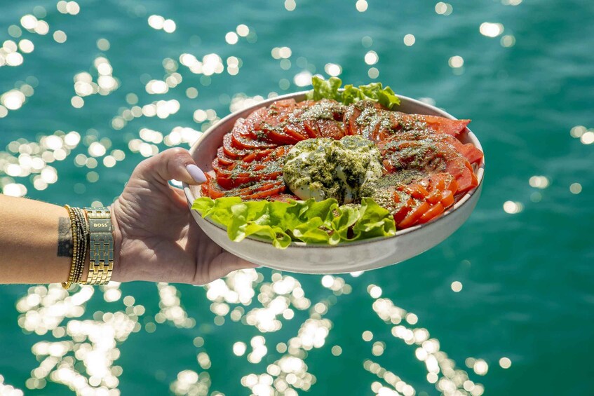 A hand holding a bowl of food with a green sauce, garnished with lettuce, over a body of water. 3