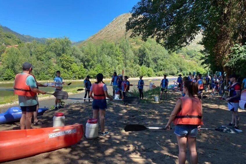 A group of people preparing for a canoeing activity by a river, with canoes and life jackets visible. 4