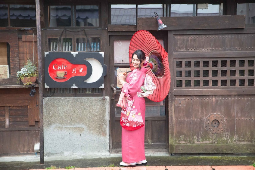 A person in traditional attire holding a fan, standing in front of a building with a sign that reads 'Cafe.' 2