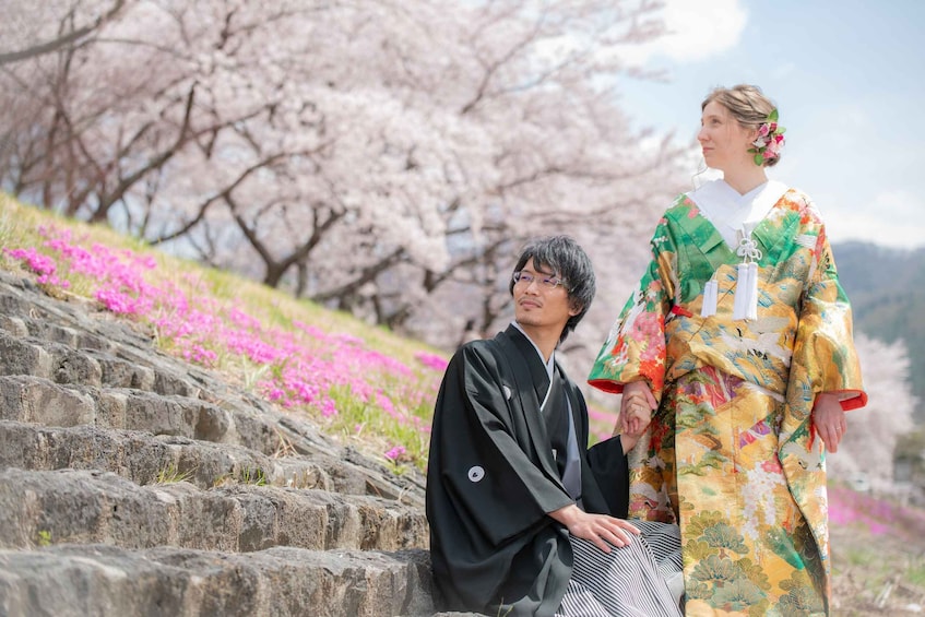Two people in traditional Japanese attire sitting on stone steps with cherry blossoms in the background. 3