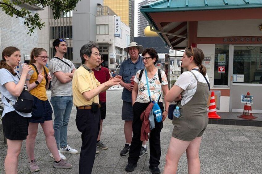 A group of people standing on a sidewalk near a building with a red awning. 2