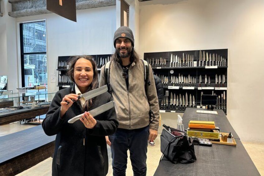 Two people in a knife shop with a display of knives behind them. 2