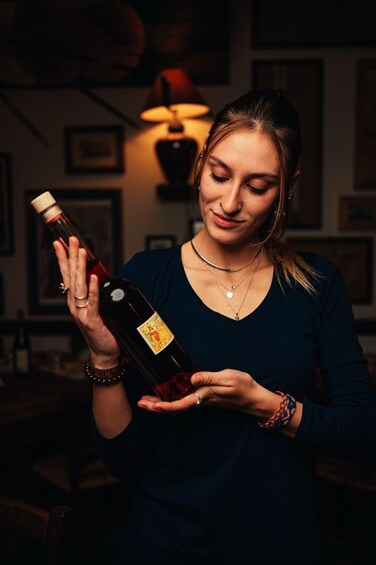 A person holding a bottle with a label, wearing a dark top, and a necklace. 4
