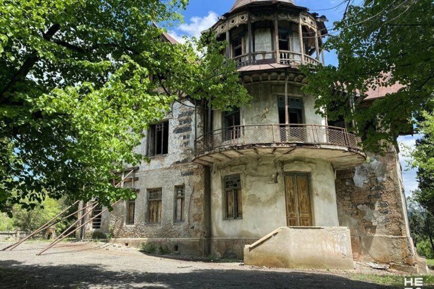 A dilapidated building with a balcony, surrounded by trees. 2