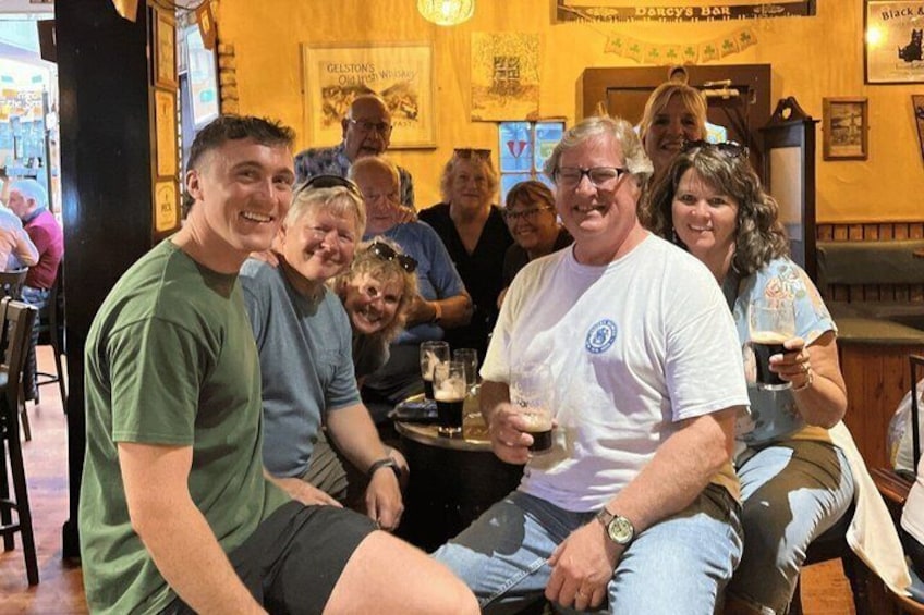 A group of people seated at a bar with drinks, a sign reading 'Black & White,' and a poster on the wall. 2