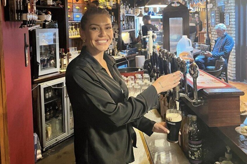 A person operating a beer tap in a bar with shelves of bottles and a refrigerator in the background. 3
