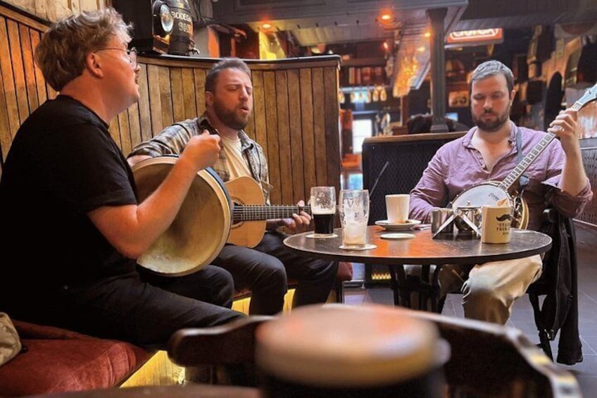 Three individuals seated at a round table with drinks, one playing a banjo. 5