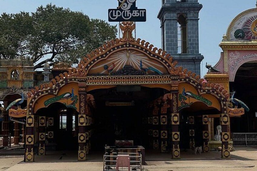 A colorful entrance with peacock statues, a clock, and a sign with Tamil script. 2