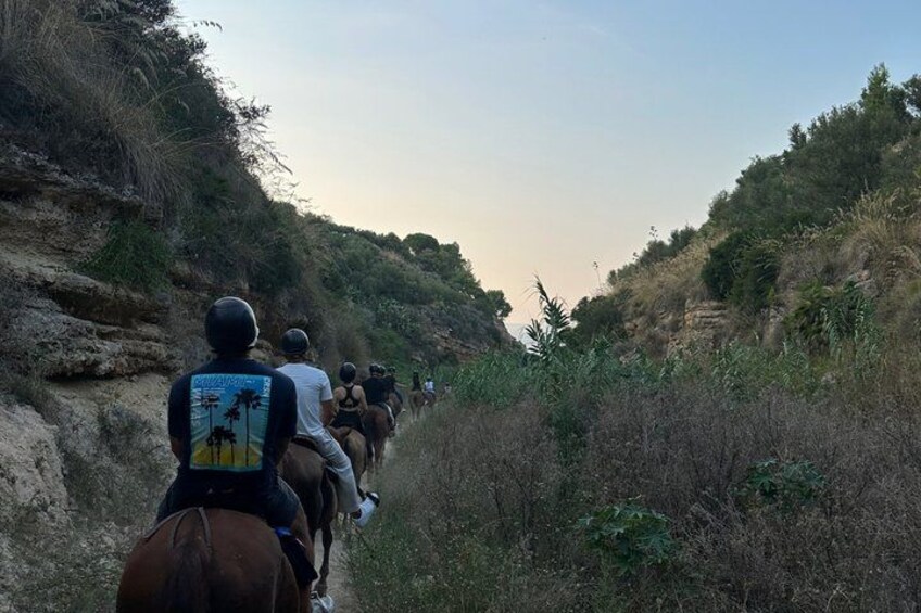 A group of people riding horses along a narrow path surrounded by hills. 2