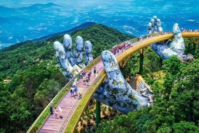 A bridge with large hand sculptures, surrounded by lush greenery and mountains. 2