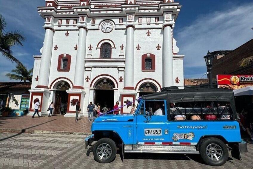 A blue off-road vehicle parked in front of a white colonial-style building with red accents and a clock. 4