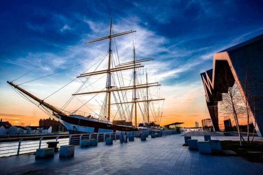 A tall ship docked at a waterfront with modern architecture in the background. 1
