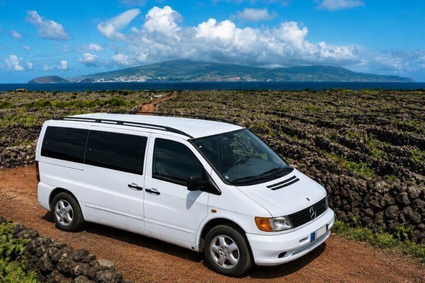 A white van parked on a dirt path with a rocky landscape and mountains in the background. 1
