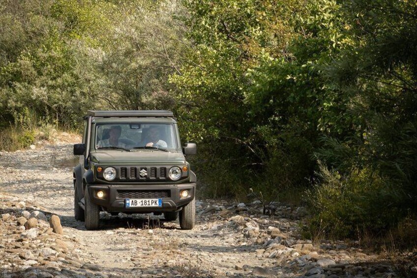 A dark-colored off-road vehicle on a rocky dirt path surrounded by dense greenery. 5