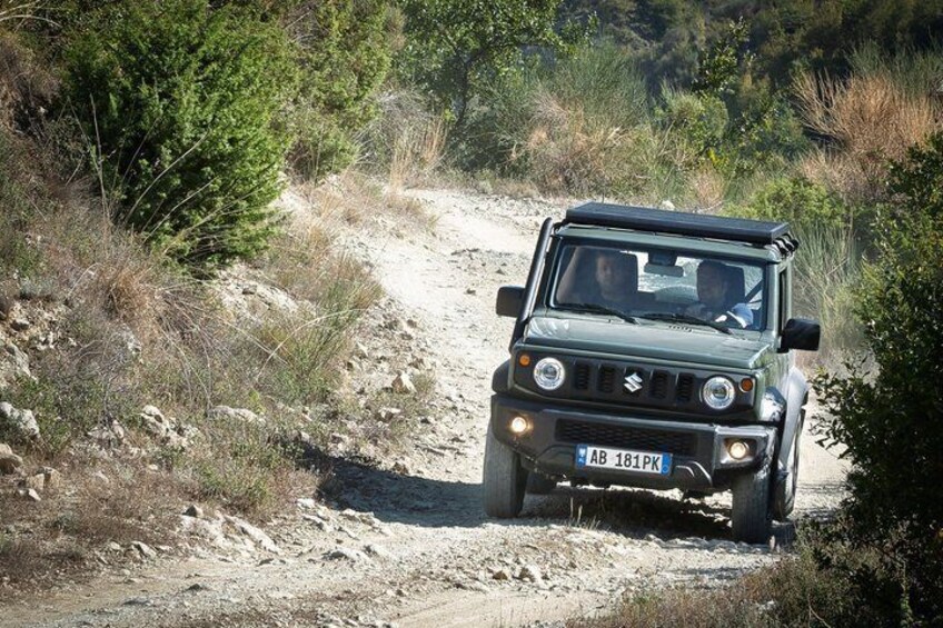 A green off-road vehicle on a dirt path surrounded by dry vegetation and trees. 2