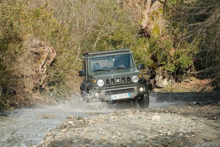 A vehicle driving through a shallow stream in a natural setting. 3