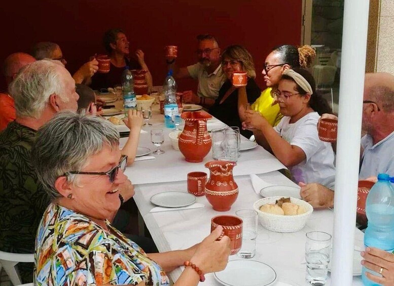 A group of people sitting around a table with red pottery, water bottles, and glasses. 5
