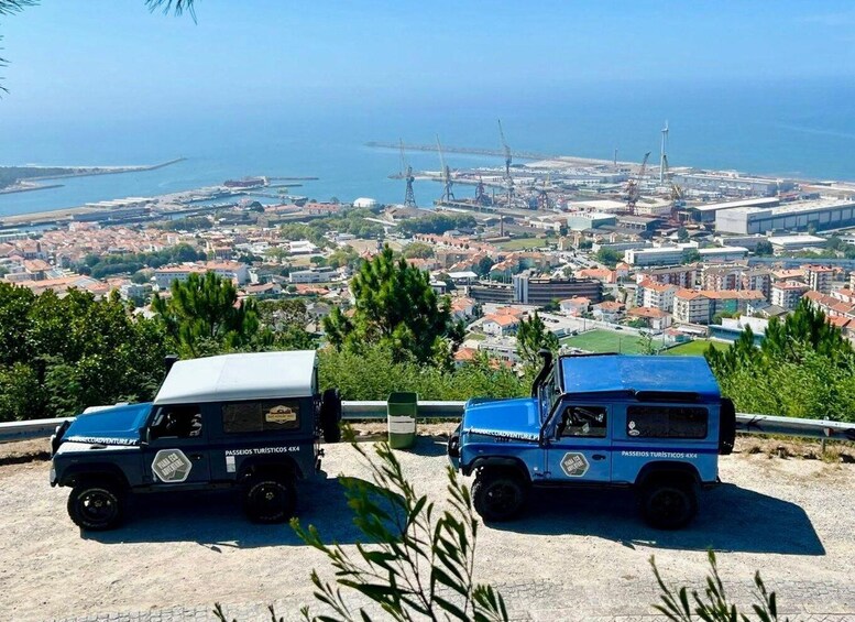 Two blue off-road vehicles parked on a coastal overlook with a view of a city and port. 3