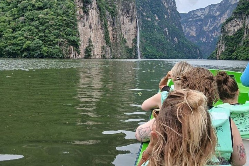 A group of people on a boat, a waterfall, and a mountainous landscape. 1