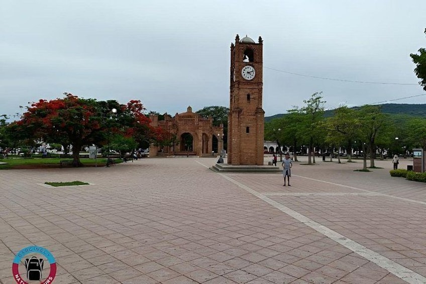 A clock tower, a paved plaza, and a tree with red leaves. 3