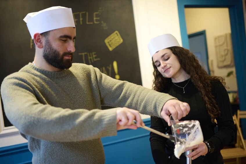 Two people wearing chef hats, one stirring a liquid in a glass. 5