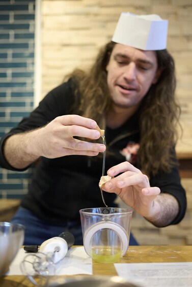 A person wearing a chef's hat holding a spoon with a liquid. 2