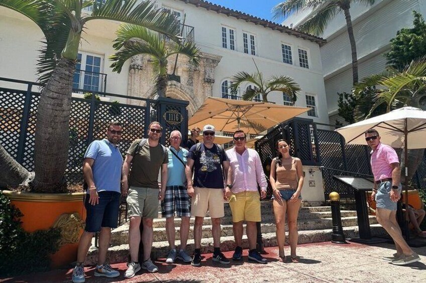 A group of people standing outdoors in a courtyard with palm trees, a fence, and a building in the background. 4
