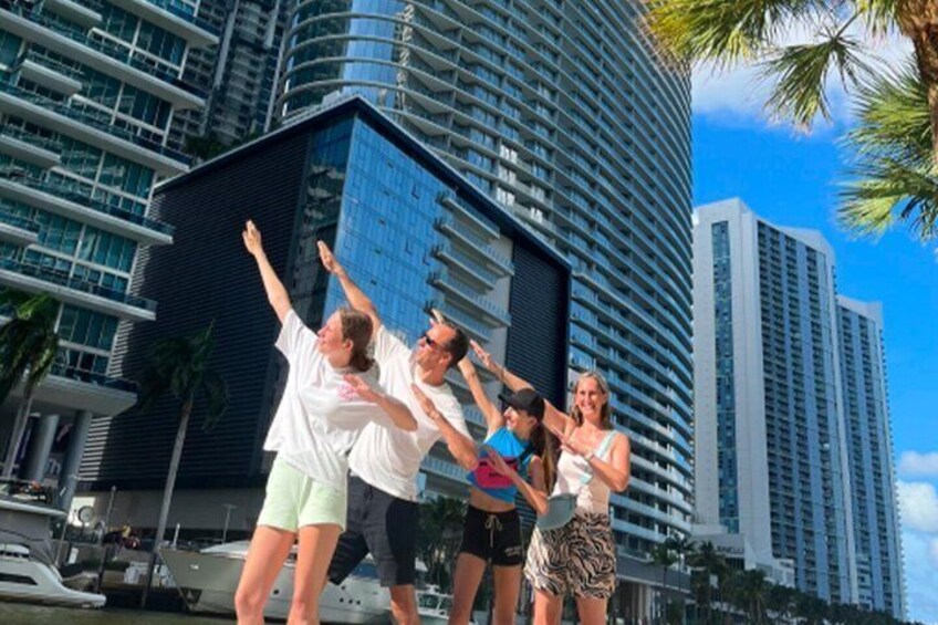 A group of people dancing in front of a modern skyscraper with palm trees and boats in the background. 3
