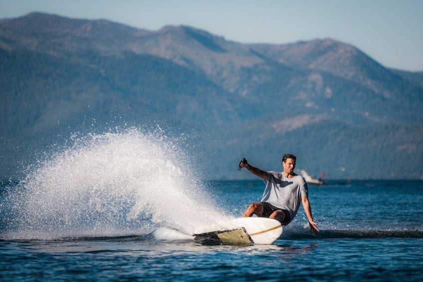 A person surfing on a wave with mountains in the background. 1