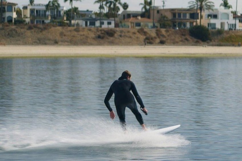 A person surfing on a calm body of water with a beach and houses in the background. 4