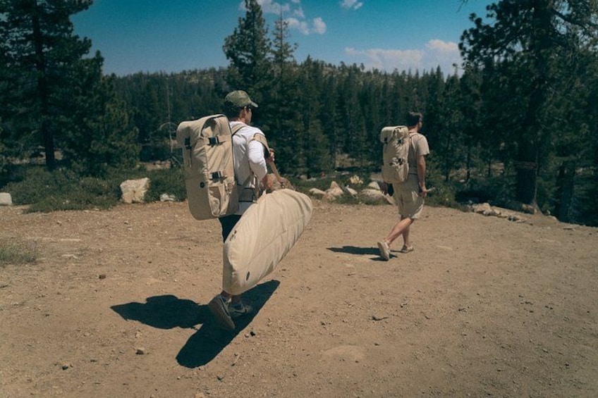 Two people carrying large bags through a forested area. 5