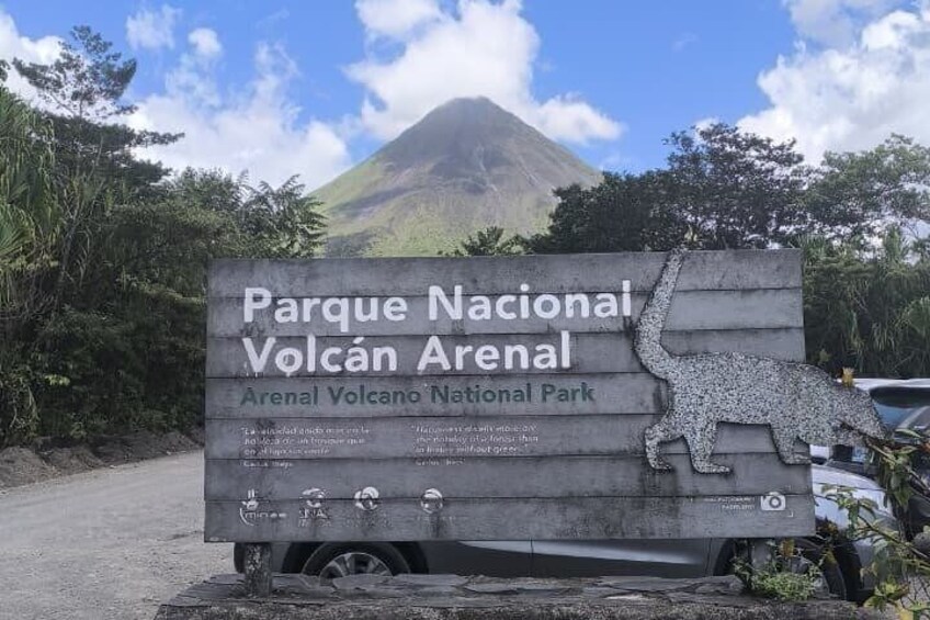 A sign for Parque Nacional Volcán Arenal with a dinosaur silhouette and a mountain in the background. 2