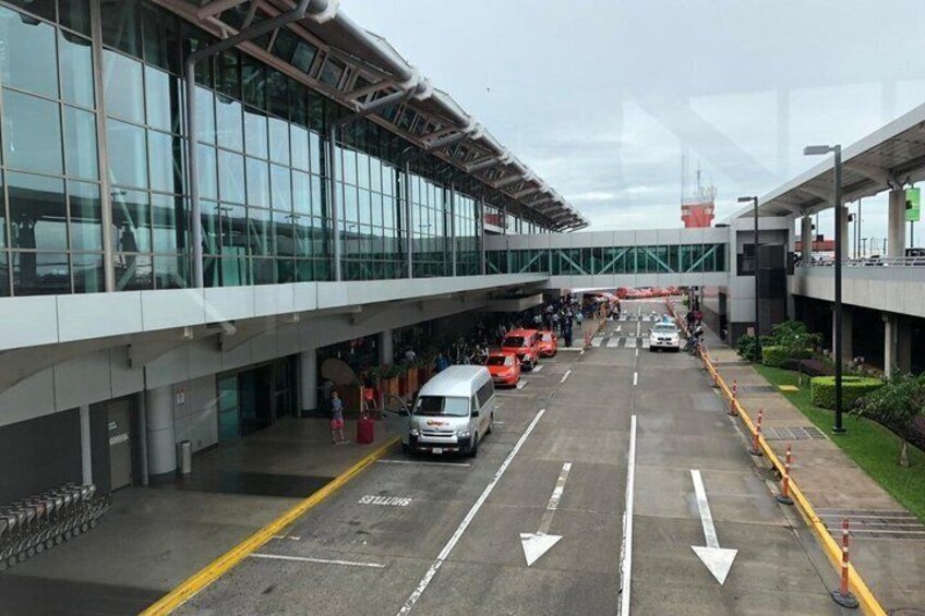 An airport terminal with glass walls, a covered walkway, and vehicles parked in the foreground. 4