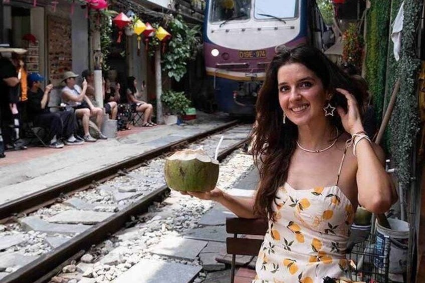 A person holding a coconut by a train track with a train in the background. 1