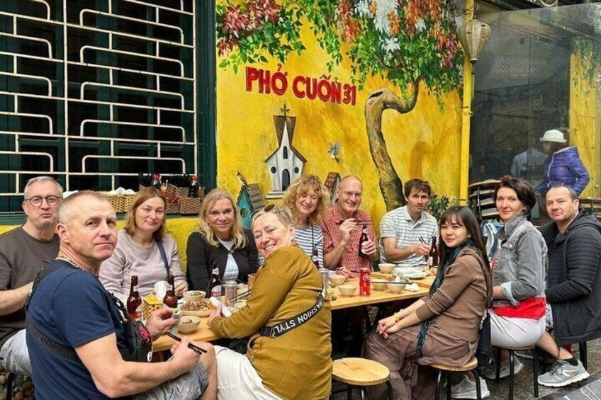 A group of people dining at an outdoor restaurant with a mural and a sign that reads 'PHÒ CUÒN 31'. 2