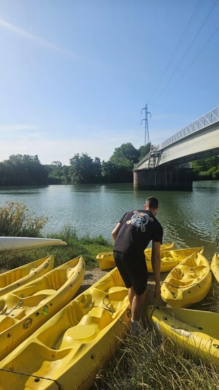 A person standing by yellow kayaks near a calm river with a bridge in the background. 2