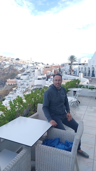 A man seated at a table with a view of a white-washed town and a hill in the background. 3