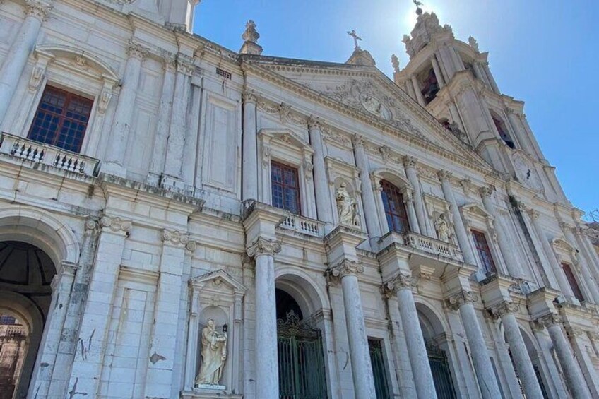 A grand historical building with ornate columns, a large arched entrance, and a bell tower. 1