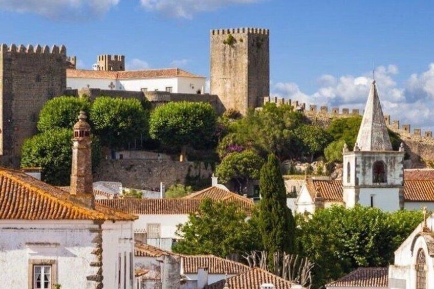 A historic town with a prominent stone tower, terracotta-roofed buildings, and a fortified wall. 3